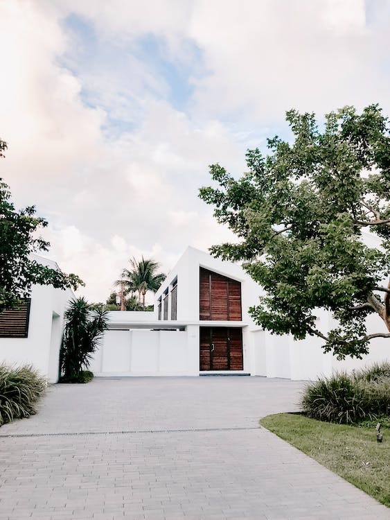 Modern, minimalist house with wooden front door, paved driveway, and simple landscaping